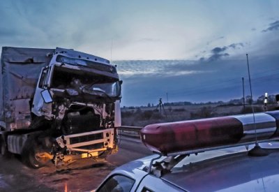 Caminhão acidentado da frente em uma estrada sendo auxiliado pelo carro de polícia
